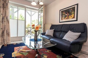 A living room with a glass coffee table, a dark leather sofa, a framed painting, and a view through a sliding glass door. - Am Stadtwald Apartment 3 - Am Stadtwald Strandstr. 15, WE 3 (Kühlungsborn)