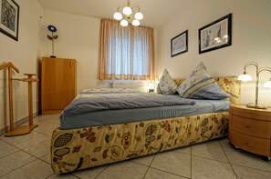 Une chambre à coucher avec un lit, une table de chevet, une lampe, des rideaux et un radiateur.