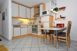 A compact kitchen with white cabinets, a microwave, a stove, and a dining table with chairs. - Am Stadtwald Apartment 3 - Am Stadtwald Strandstr. 15, WE 3 (Kühlungsborn)