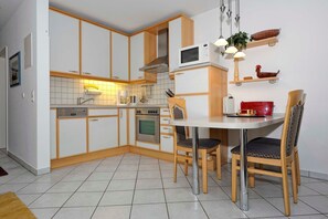 Une cuisine compacte avec des meubles blancs, un four à micro-ondes, une cuisinière et un coin repas comprenant deux chaises et une table.