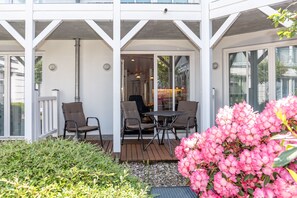 A covered outdoor seating area with chairs and a table, surrounded by greenery and pink flowers. - Am Stadtwald Apartment 3 - Am Stadtwald Strandstr. 15, WE 3 (Kühlungsborn)
