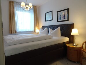 A hotel room with a bed, a nightstand, a lamp, a chair, and two framed pictures on the wall. - Am Stadtwald Apartment 3 - Am Stadtwald Strandstr. 15, WE 3 (Kühlungsborn)