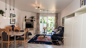 Un salon moderne comprenant un coin repas, un canapé, une table basse et un téléviseur. Il y a une grande fenêtre avec des rideaux, un luminaire au plafond et une plante sur le rebord de la fenêtre.