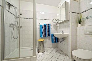 A bathroom with a glass-enclosed shower, a sink, a toilet, and a trash can. - Am Stadtwald Apartment 3 - Am Stadtwald Strandstr. 15, WE 3 (Kühlungsborn)