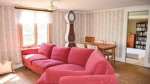 Ein Wohnzimmer mit einem roten Sofa, einem Holzesstisch mit Stühlen, einer Uhr und einem Bücherregal.