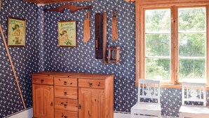 Ein Zimmer mit einem Holzkabinett, blumigem Wandpapier und einem Fenster mit Blick ins Grüne.