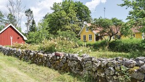 Eine ländliche Landschaft mit einer Steinmauer, einem roten Bauernhof und einem gelben Haus mit rotem Dach.