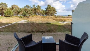 En balkon med fletstole og et bord, der udover en græsplæne med træer og et vandareal.