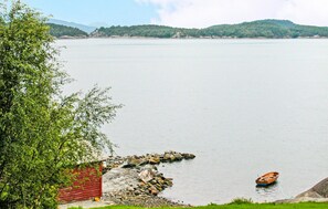 Ein ruhiger See mit einem hölzernen Boot, einem roten Gebäude und einem Baum am Ufer.
