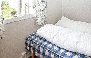 Ein Schlafzimmer mit Bett, einem Fenster mit Vorhängen und Blick ins Freie.
