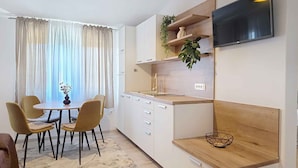 Une cuisine moderne avec des meubles blancs, un plan de travail en bois, un téléviseur encastré et un coin repas avec deux chaises.