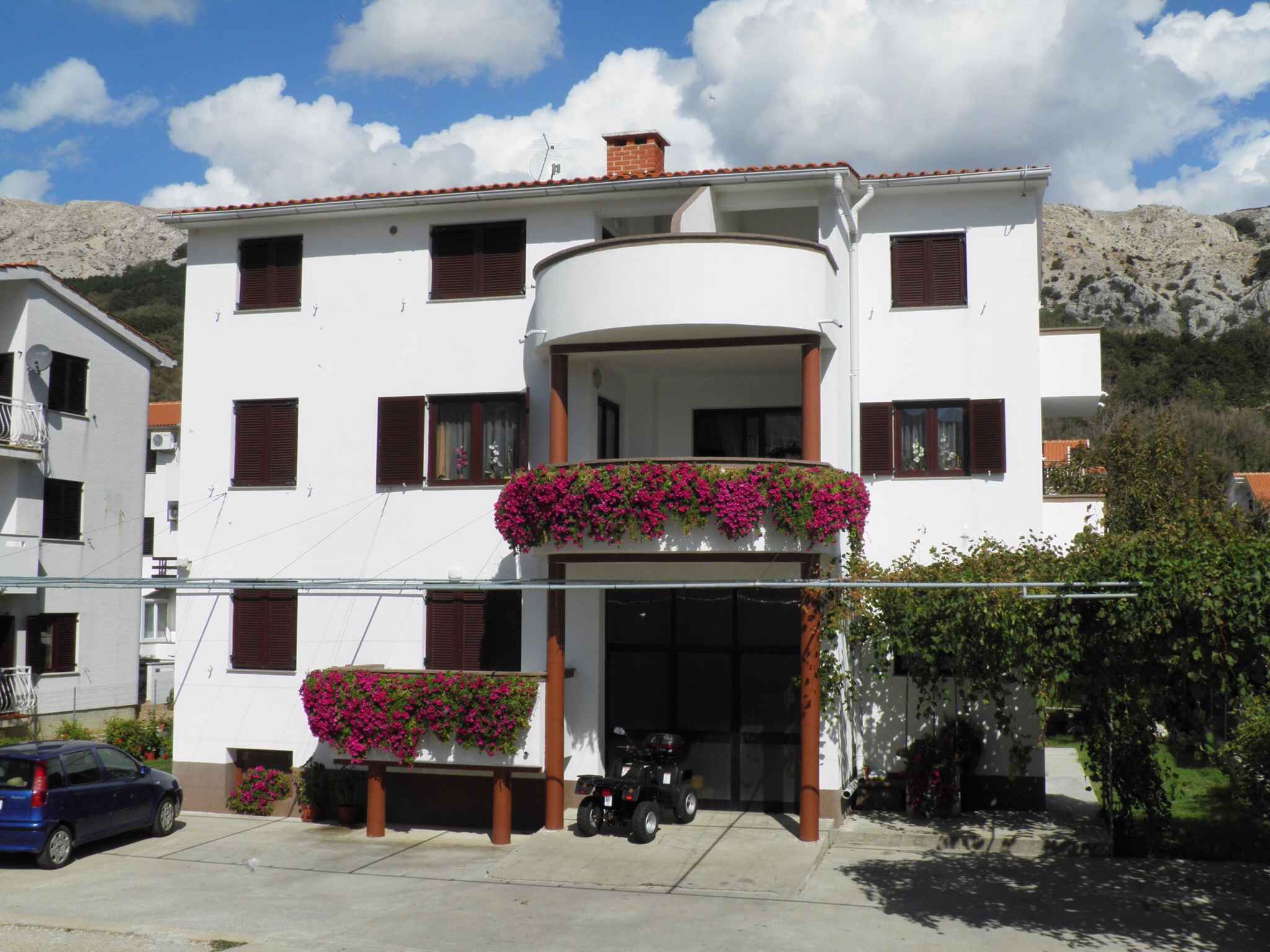 A two-story building with a balcony adorned with flowers, a garage, and a parked car.