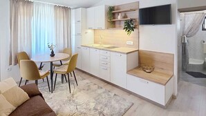 Une cuisine moderne avec des meubles blancs, une table à manger avec des chaises, un téléviseur fixé au-dessus du comptoir et un espace douche.