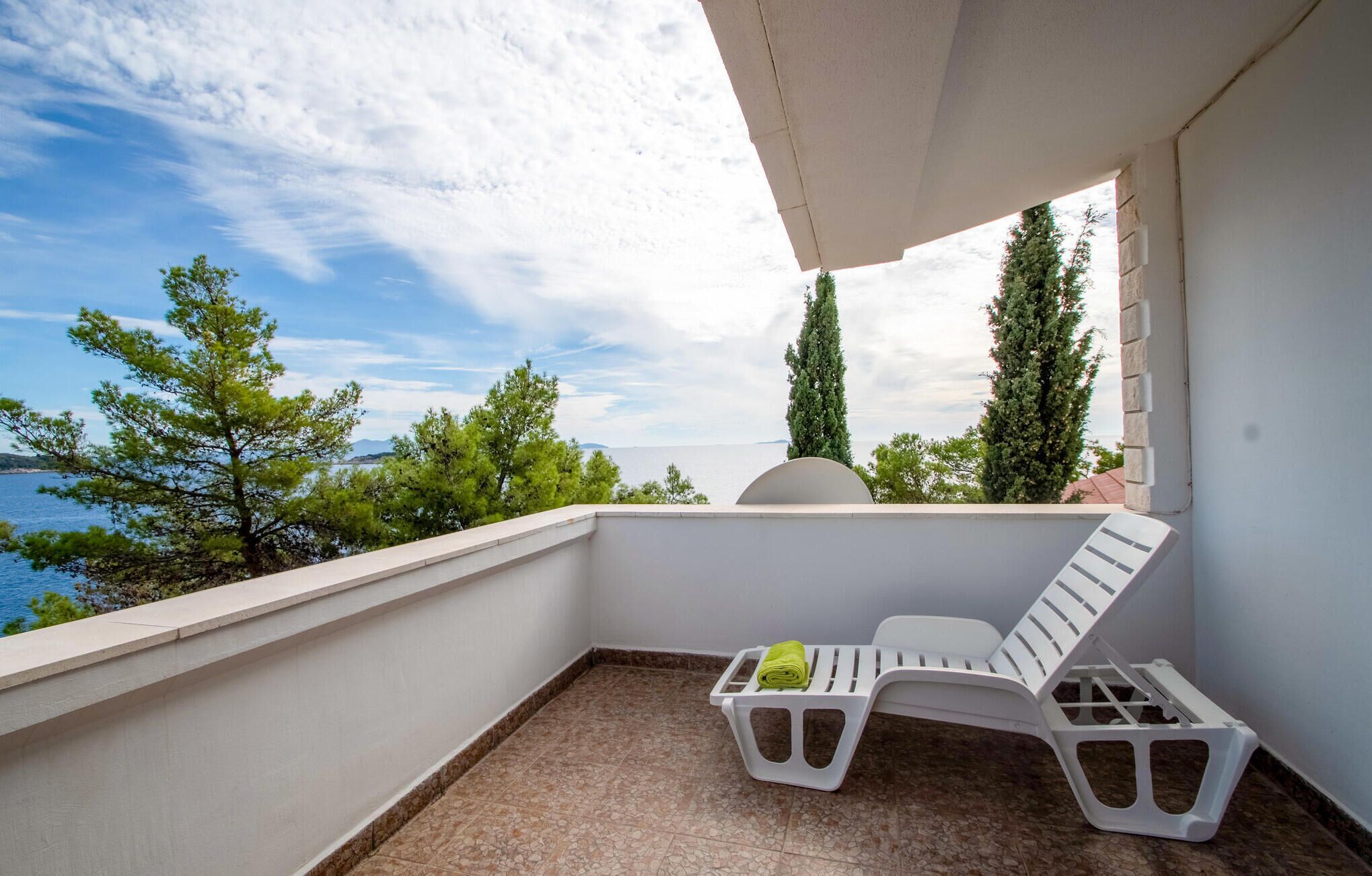 A balcony with a white chair and a small table, overlooking a body of water and trees.