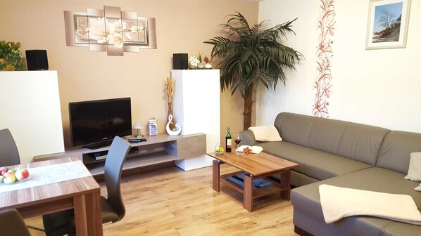 A living room with a TV, sofa, coffee table, and a plant.