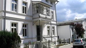 A two-story building with a balcony on the second floor, a front entrance with steps, and a car parked in front. - Apartment I - Villa Elfriede (Sassnitz)