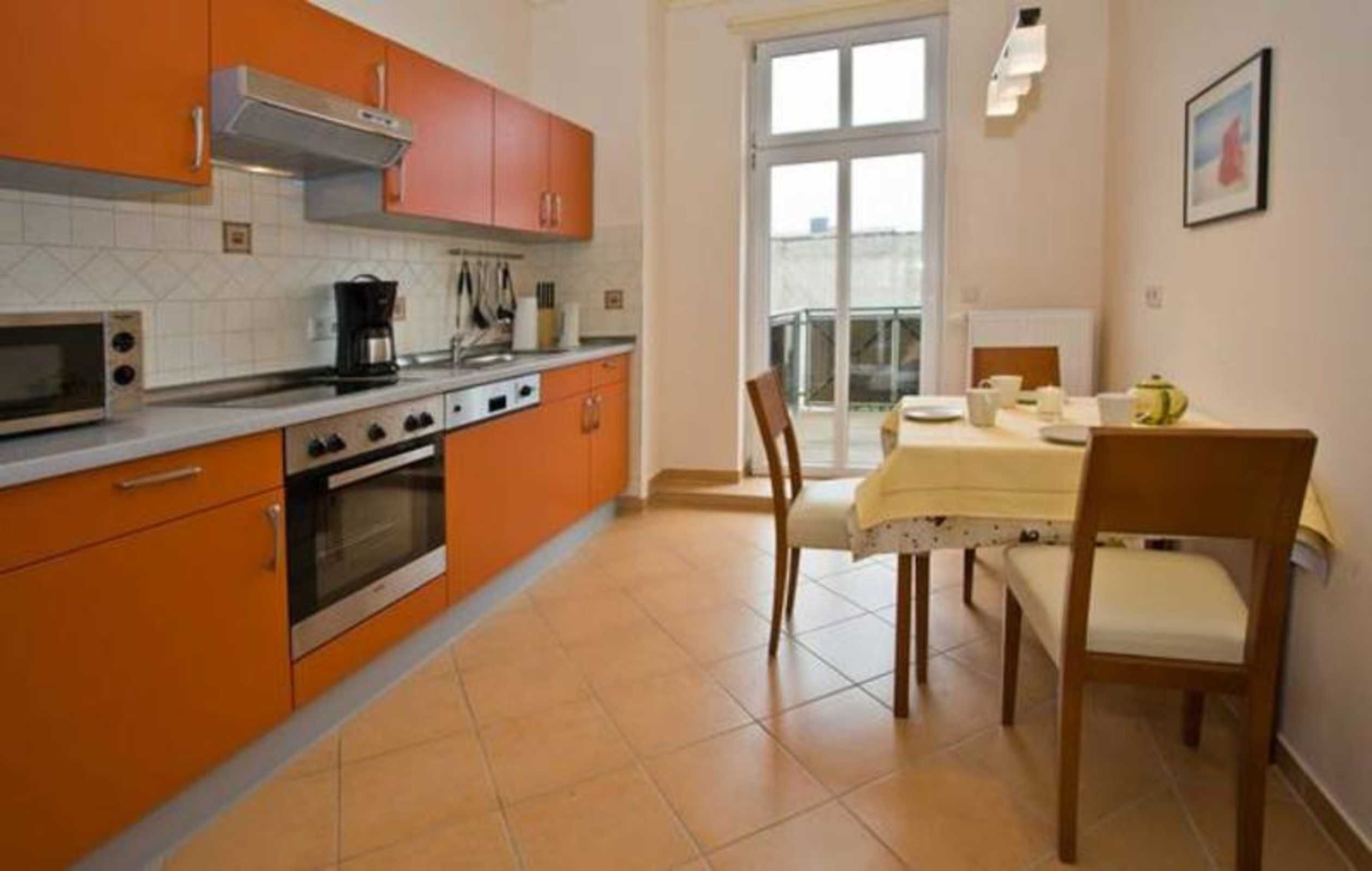 A kitchen with orange cabinets, a stove, and a dining area with a table and chairs.