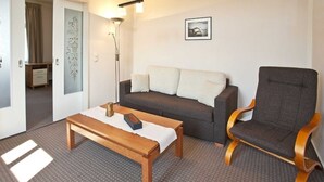 A room with a dark brown sofa, a wooden bench, a grey armchair, a floor lamp, and a framed picture on the wall. - Apartment I - Villa Elfriede (Sassnitz)