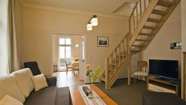 A living room with a sofa, a wooden table, a TV, and a staircase. - Apartment I - Villa Elfriede (Sassnitz)