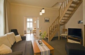Un salon avec un canapé, une table en bois, un téléviseur et un escalier.