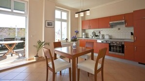 A modern kitchen with orange cabinets, a dining table with chairs, and a large window providing natural light. - Apartment I - Villa Elfriede (Sassnitz)
