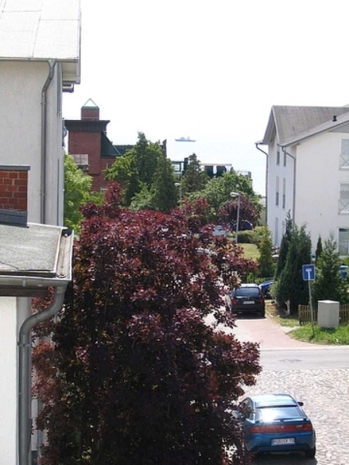 A residential street with houses, a parked car, and a T-shaped sign.