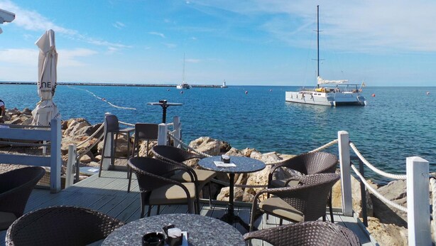 Ein Restaurant direkt am Meer mit Terrassensitzplätzen, Blick auf das Meer und Booten im Hintergrund.