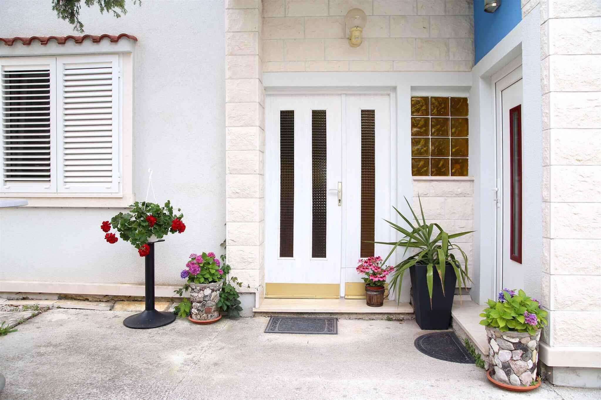 A building entrance with a white door, a small window with shutters, and potted plants.