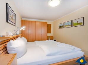 Una habitación de hotel con una cama, un armario de madera, un escritorio con una lámpara y tres cuadros en la pared.
