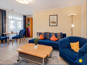 Una sala de estar con un sofá azul, una mesa de centro de madera y un comedor con una mesa y sillas.