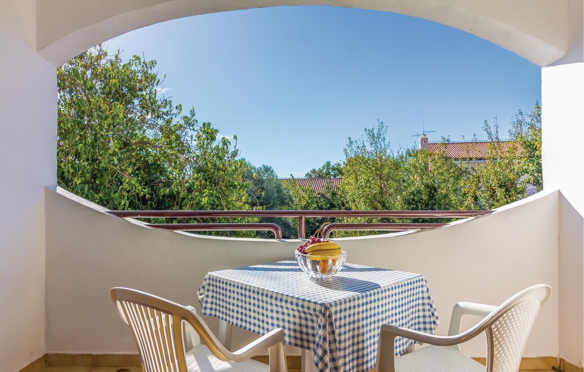 A balcony with a table and chairs, a bowl of fruit, and a view of trees and buildings.