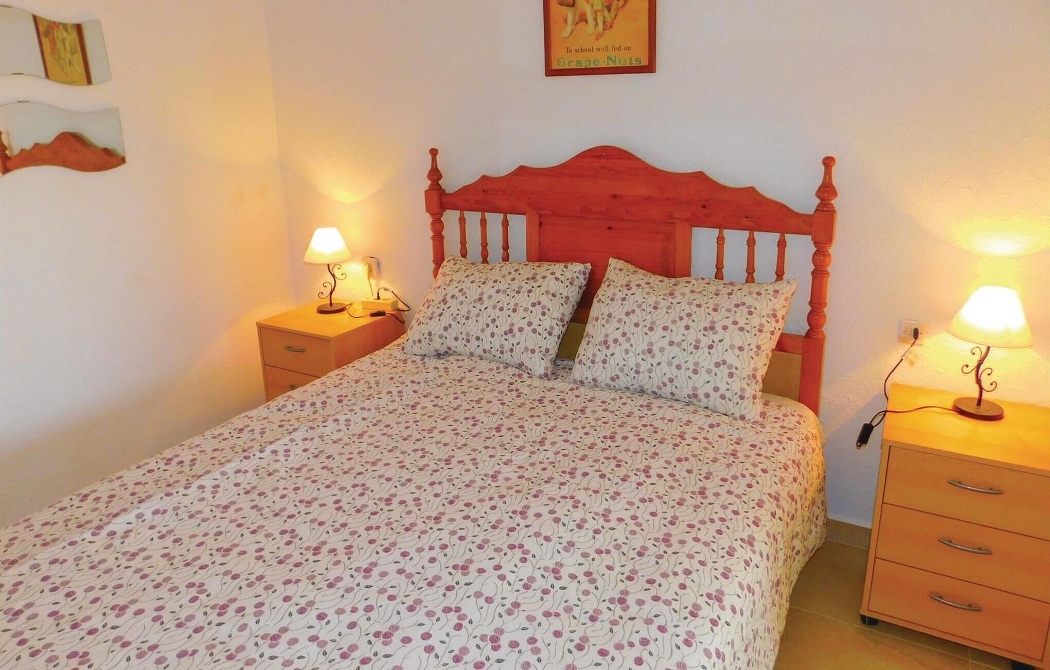 A bed with floral bedding, two bedside lamps, and a wooden headboard.
