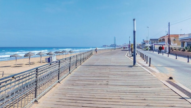 Een houten looppad naar het strand met parasols en een hekwerk.