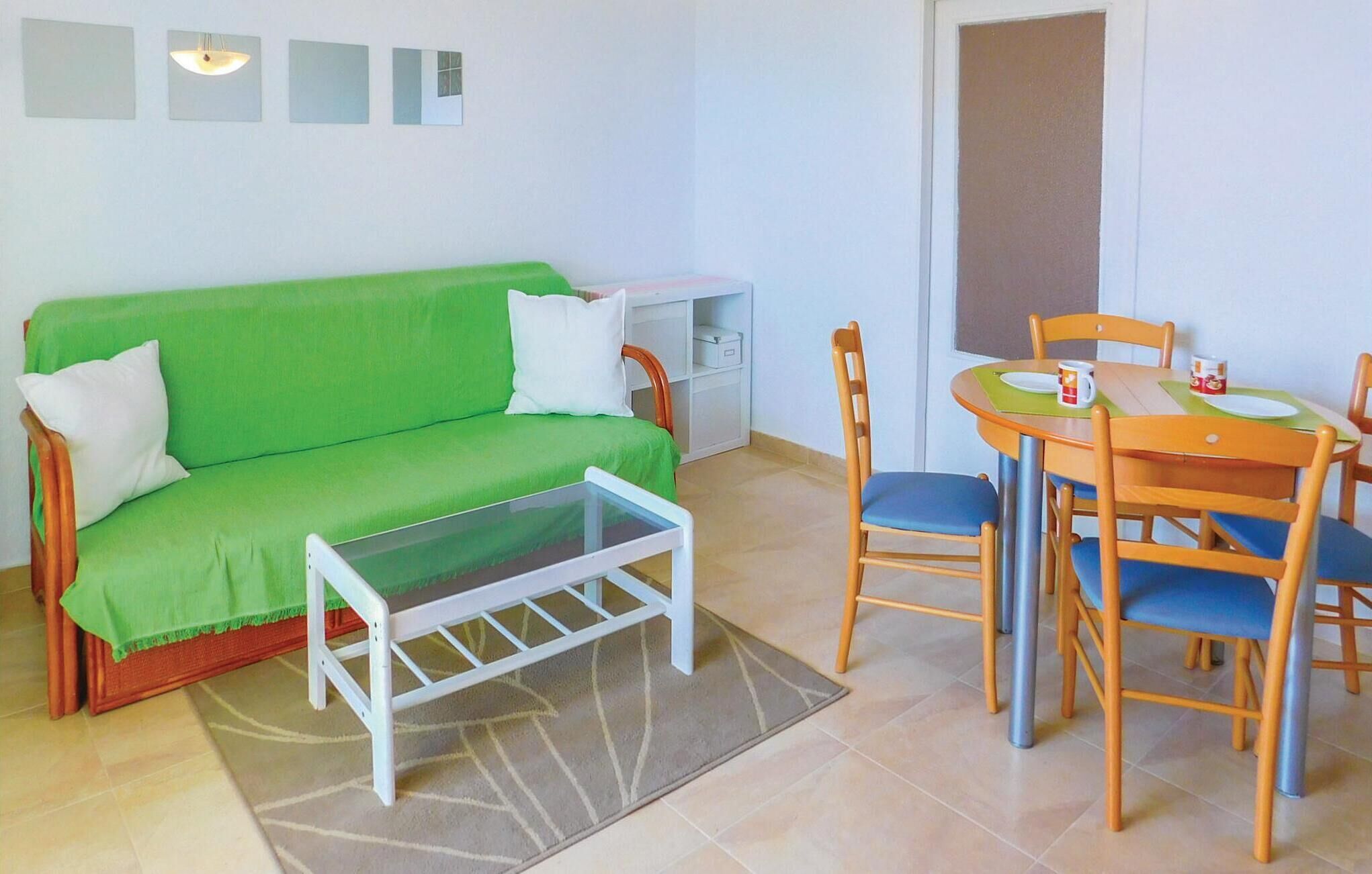 Une petite pièce lumineuse, avec un canapé vert, une petite table entourée de chaises et un meuble blanc.