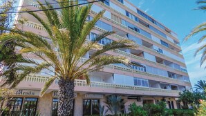 Een hotel met meerdere verdiepingen, balkons, palmbomen en een heldere lucht.