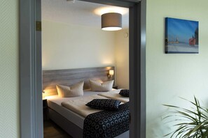 Une chambre d’hôtel avec un lit, des oreillers, une lampe, un tableau au mur et une plante.