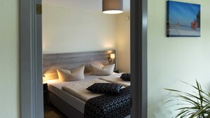 Une chambre d’hôtel avec un lit, des oreillers, une lampe, un tableau au mur et une plante.