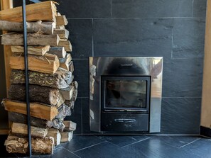 Una chimenea moderna con un revestimiento de piedra negra, leña apilada a la izquierda y una puerta metálica.