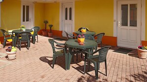 An outdoor patio with multiple round tables and chairs, surrounded by yellow walls and white doors.