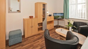 A modern living room with a wooden cabinet, a television, a small table with a vase, and a window with curtains.