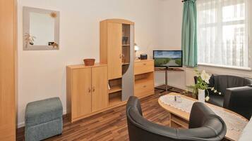 Ein modernes Wohnzimmer mit einem Holzkasten, einem Fernseher, einem kleinen Tisch mit einer Vase und einem Fenster mit Vorhängen.