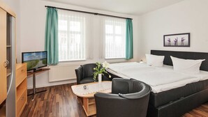 A modern hotel room with a large bed, a desk with a computer, a chair, and a small table with a vase of flowers.