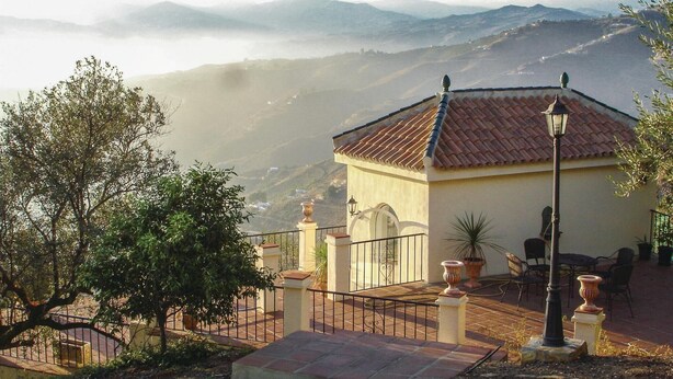 Ein Gebäude mit einem Ziegeldach, einem Balkon mit Geländer und Blick auf ferne Berge.