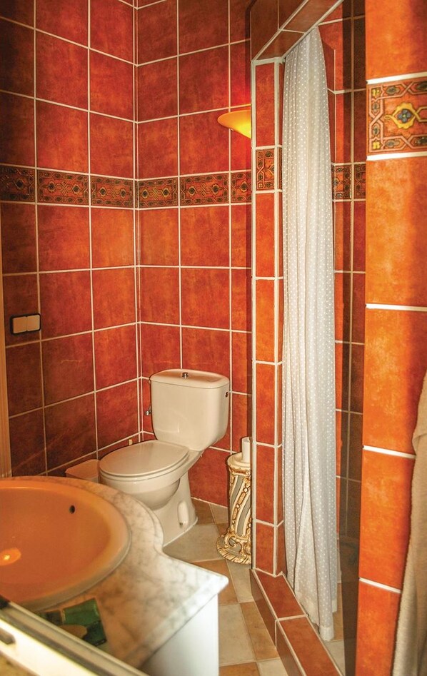 A bathroom with red tiled walls, a white toilet, a sink with a marble basin, and a shower curtain. - Amazing home in Algarrobo (Algarrobo)