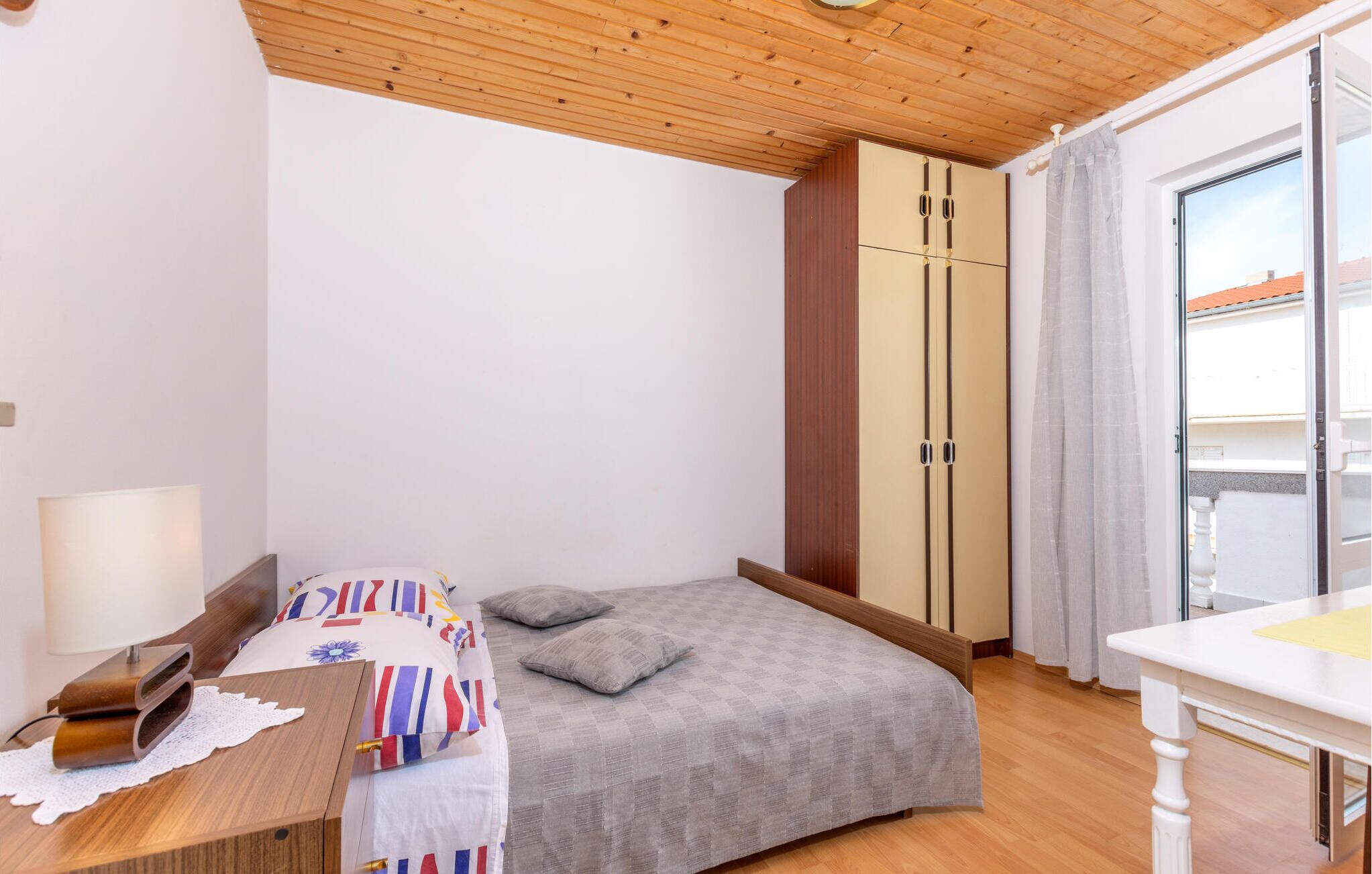 A bedroom with a bed, a desk, a lamp, and a wardrobe.