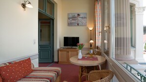 En hyggelig stue med en sofa, et lille bord med en vase blomster, et fjernsyn og et vindue med udsigt.