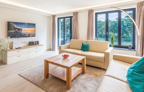 A modern living room with a sofa, a coffee table, a TV, and large windows with curtains.