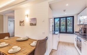 A modern kitchen with a large window, a dining area with a wooden table set for four, and a view of the outdoors.