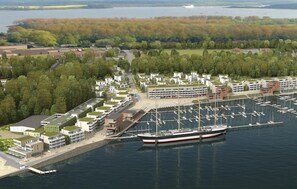 An aerial view of a marina with modern buildings, boats, and a forested area in the background. - Priwallpromenade 2, Whg 3 (Travemünde Waterfront)