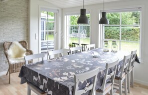 A dining area with a large table covered in a patterned tablecloth, surrounded by white chairs. There are two hanging pendant lights above the table. - Nice home in Hadsund with WiFi (Hadsund)